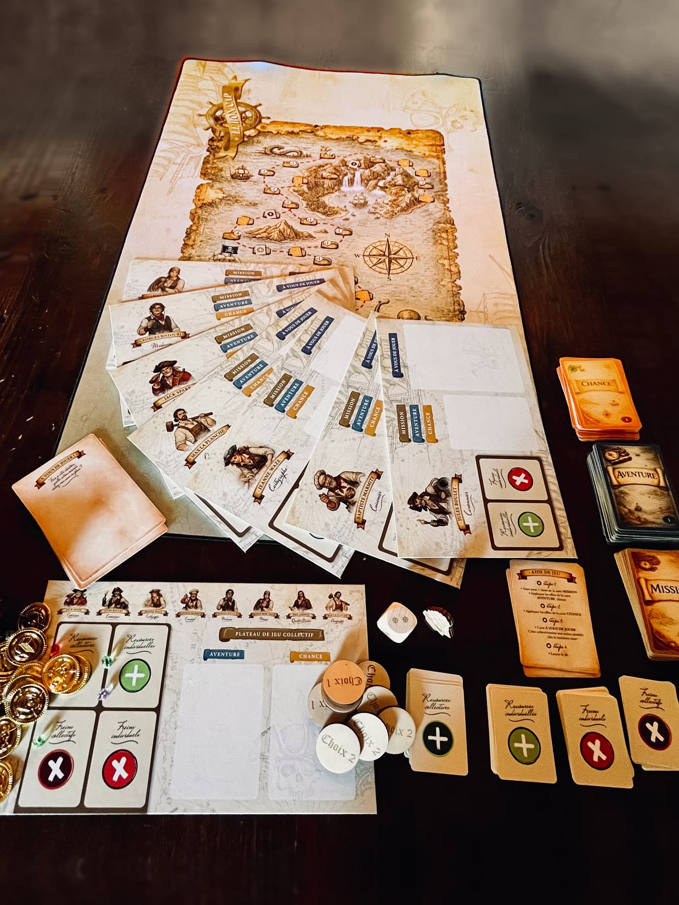Le jeu installé sur une table : le tapis carte au trésor, les plateaux des huit personnages, les cartes, les jetons de vote et les pièces d’or.